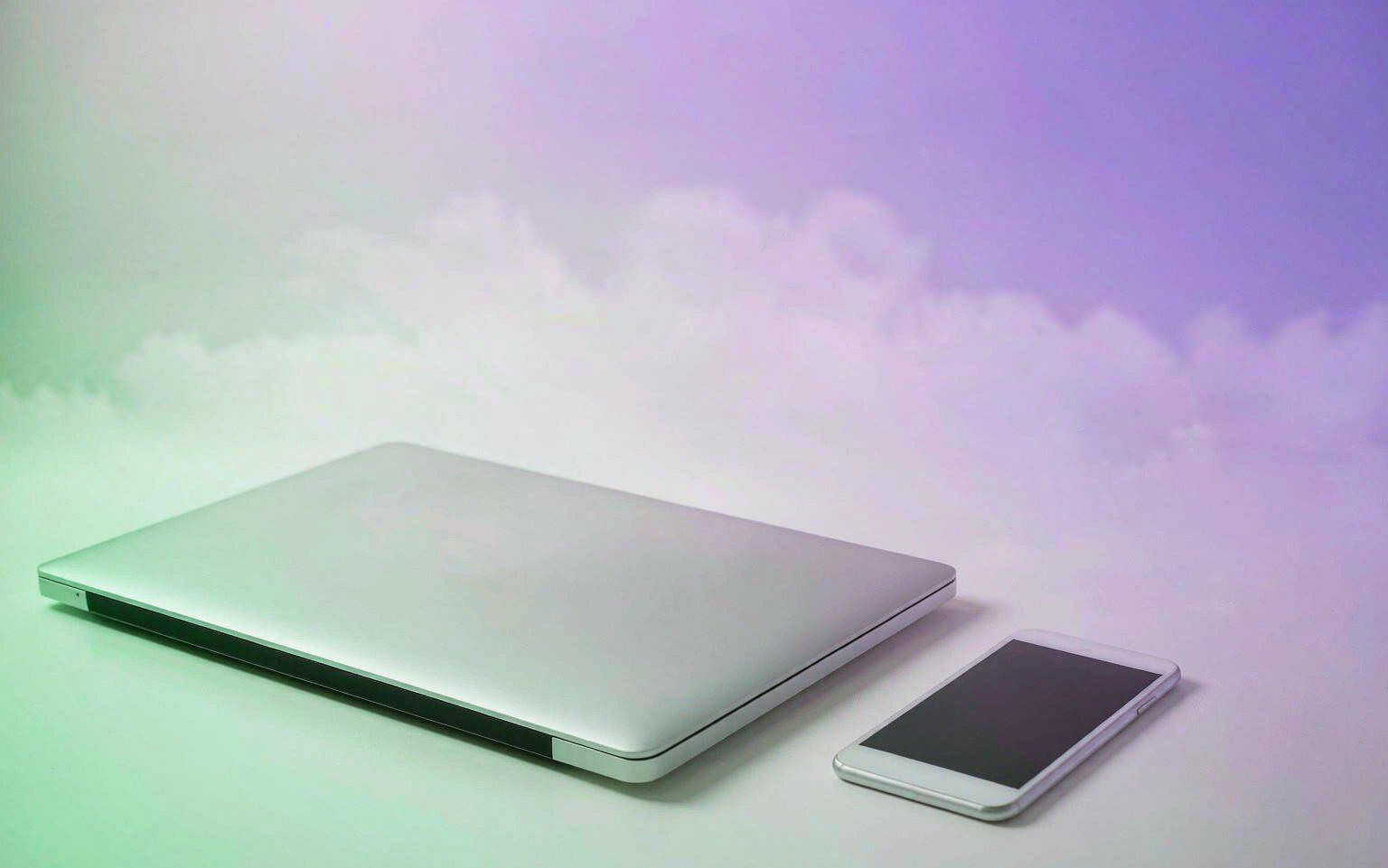 Laptop and smartphone on a bright minimal desk with purple and mint light